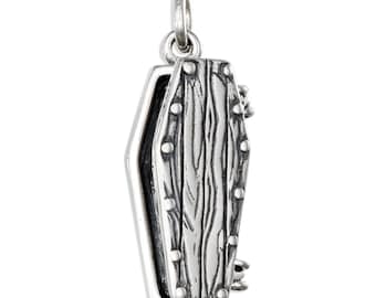 May include: A silver coffin-shaped pendant with a hinged lid. The pendant has a detailed wood grain texture on the front and is accented with small, round rivets. The bail is a simple loop for attaching to a chain.
