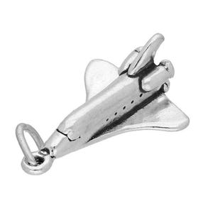 Puede incluir: Un amuleto de plata con forma de transbordador espacial. El amuleto tiene un bucle en la parte superior para sujetarlo a una pulsera o collar.