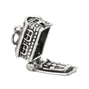 May include: A silver-colored charm in the shape of a house with an open door. The charm has detailed brickwork and a hinged door that opens to reveal a small interior. The charm is designed to be attached to a bracelet or necklace.