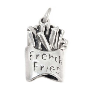 May include: A silver-toned charm in the shape of a container of French fries. The container has the words "French Fries" engraved on the front. The charm has a loop at the top for attaching to a necklace or bracelet.