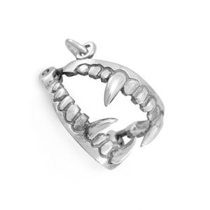Puede incluir: Colgante plateado con forma de mandíbula de vampiro con colmillos afilados. El colgante tiene un lazo para una cadena. Los dientes están detallados y el metal tiene un acabado pulido. El diseño es gótico y atrevido.