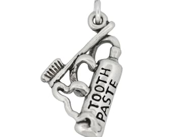 May include: A silver-toned charm featuring a toothbrush, a tube of toothpaste, and decorative swirls. The toothpaste tube is labeled "TOOTH PASTE". The charm is designed to be attached to a necklace or bracelet.