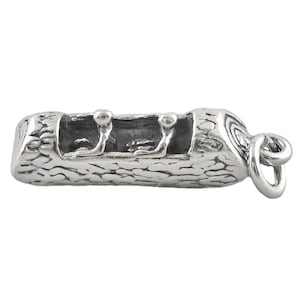 May include: A silver canoe charm featuring two figures. The charm has a textured, wood-like exterior and a loop for attaching to a bracelet or necklace. The canoe's interior is smooth and dark.