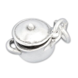 May include: Silver charm in the shape of a small pot with a lid. The pot has two handles and a round lid. The charm is designed to be attached to a bracelet or necklace.