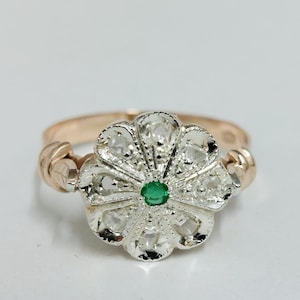 Puede incluir: Un anillo de plata con un diseño de flor engastado con pequeñas piedras blancas y una piedra preciosa verde en el centro. La banda del anillo es de oro rosa.