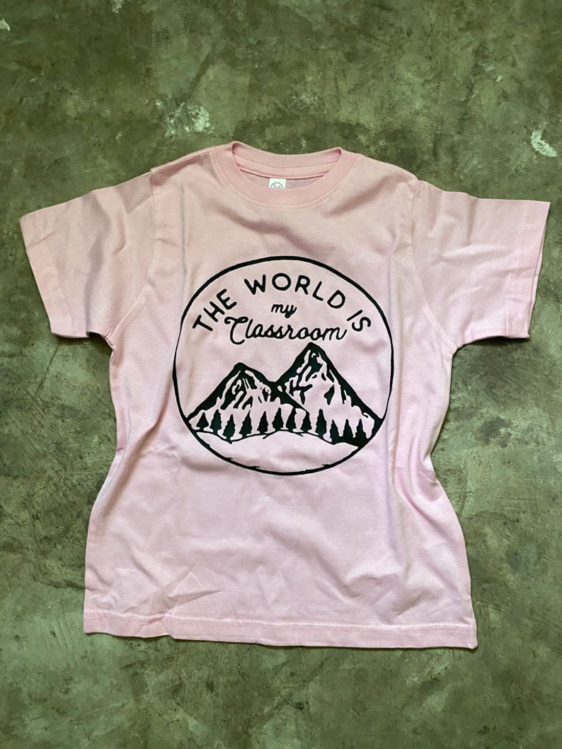 May include: Pink t-shirt with a black circle graphic that says "The World is my Classroom" with a mountain range inside the circle.
