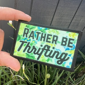 May include: A black and green patch with white text that reads "Rather Be Thrifting". The patch has a floral pattern.