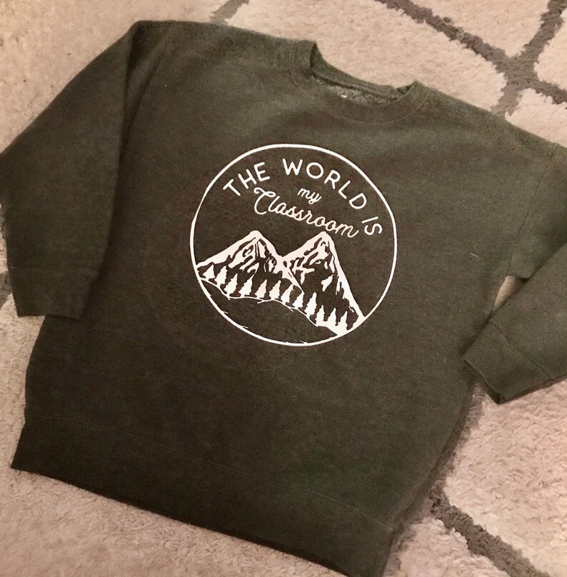May include: A dark green sweatshirt with a white circle graphic featuring two mountains and the text "THE WORLD IS my CLASSROOM".