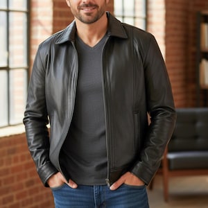 May include: Black leather jacket with a collared neckline and a front zipper closure. The jacket has a classic design with a tailored fit, featuring a v-neck shirt underneath. The model is wearing blue jeans.