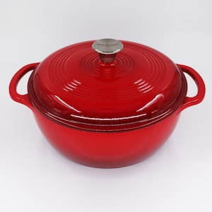 Puede incluir: Cazuela de hierro fundido roja con tapa y dos asas. La tapa tiene un pomo plateado con las palabras "Made in China" en ella.