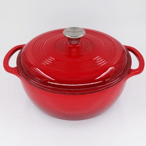 Puede incluir: Cazuela de hierro fundido roja con tapa y dos asas. La tapa tiene un pomo de acero inoxidable con las palabras "Kitchen Craft" grabadas.