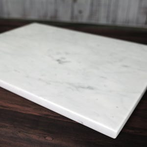 May include: White marble cutting board with a smooth surface and slightly rounded edges.