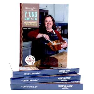 May include: A stack of four blue cookbooks with the title "Y'UNS COME & EAT" and the logo "MOUNTAIN COOKIN' with Missy" on the cover. The top book features a woman in a blue apron holding a wooden bowl.