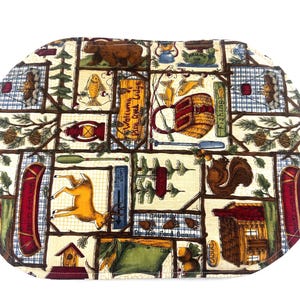 May include: An oval-shaped placemat with a cabin theme. The placemat features a patchwork design with images of a bear, fish, a deer, a squirrel, a canoe, and a cabin. The text "Welcome to Pine Creek Lodge" is visible.