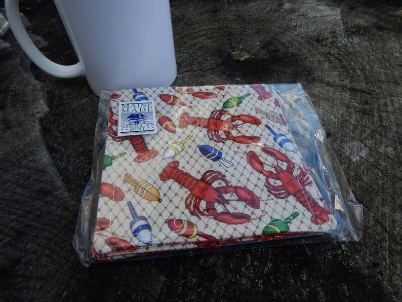 Puede incluir: Un juego de cuatro posavasos de tela blanca con un dise&ntilde;o de langosta y boya. Los posavasos est&aacute;n empaquetados en una bolsa de pl&aacute;stico transparente y llevan una etiqueta "Maine Made".