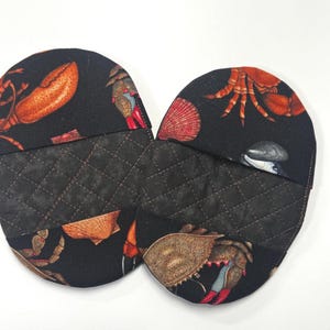 May include: Two oven mitts with a black background and a quilted pattern. The mitts are decorated with illustrations of various sea creatures, including lobsters, crabs, and seashells in shades of orange, red, and brown.