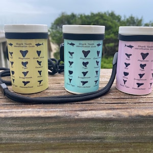 May include: Three ceramic travel mugs in yellow, teal, and pink, each with a white lid and black band. The mugs feature a shark tooth identification guide with various shark tooth illustrations and the text "Shark Tooth Identification Guide."
