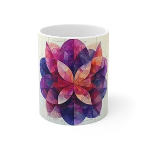May include: A white ceramic coffee mug featuring a colorful floral design. The design is a symmetrical pattern of overlapping petals in shades of purple, pink, and orange. The mug has a standard cylindrical shape.