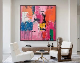 Könnte beinhalten: Großformatiges, gerahmtes abstraktes Gemälde mit kräftigen Farben. Das Kunstwerk zeigt breite Pinselstriche in Rosa, Orange, Blau, Grün und Gelb. Das Gemälde hängt über zwei weißen Sesseln und einem kleinen Tisch in einem modernen Wohnzimmer.