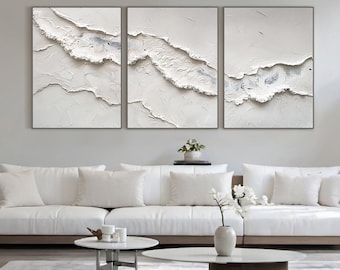 May include: A triptych of abstract textured art pieces. Each framed canvas features a white, layered design with subtle gray accents, resembling a topographical map or a stylized wave. The artwork is displayed above a white sofa in a modern living room.