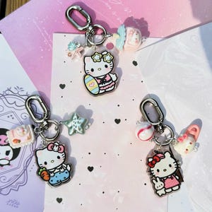 May include: Three Hello Kitty keyrings with silver clasps. Each keyring features a different Hello Kitty design, including one with an Easter egg, one with a carrot, and one with a baseball. Additional charms include a star, a drink, and a shoe.