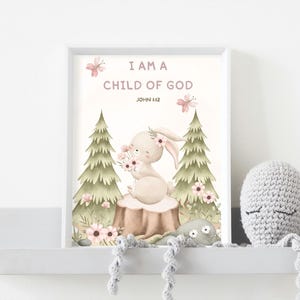 May include: A framed art print with the text "I AM A CHILD OF GOD" and a watercolor illustration of a bunny holding flowers. The artwork features a soft color palette with pink and green accents. A crocheted octopus toy is on the shelf.