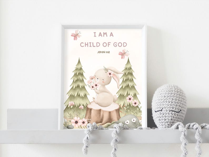May include: A framed art print with the text "I AM A CHILD OF GOD" and a watercolor illustration of a bunny holding flowers. The artwork features a soft color palette with pink and green accents. A crocheted octopus toy is on the shelf.