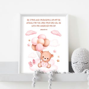 Framed teddy bear scripture art featuring Joshua 1:9 displayed on a white shelf with a gray crocheted octopus plushie, showing ideal placement in a baby’s nursery decor.