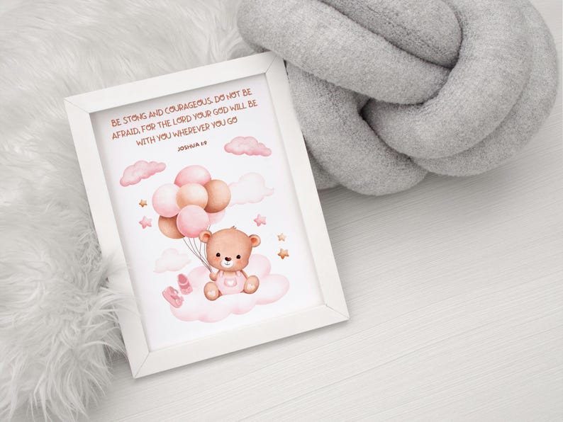 Flat-lay of a framed nursery print with a teddy bear holding balloons, featuring Joshua 1:9. Set against a white wood background with gray and white cozy textures for a soft, comforting presentation.