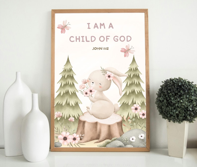 Framed nursery wall art with a bunny holding flowers and the verse "I Am a Child of God – John 1:12." Displayed on a white shelf between two white ceramic vases and a small potted plant, perfect for gender-neutral nursery decor.