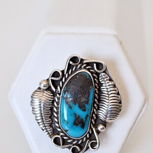 May include: A silver ring with a turquoise stone set in a detailed design. The stone is a vibrant blue with black veins.