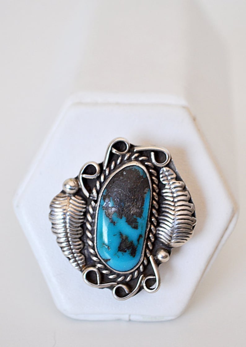 May include: A silver ring with a turquoise stone set in a detailed design. The stone is a vibrant blue with black veins.