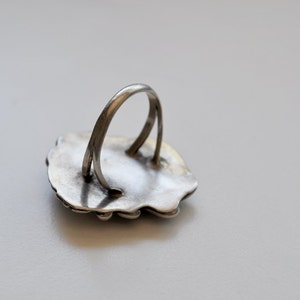May include: Silver ring with a detailed design on the front. The back of the ring is plain and shows the band.