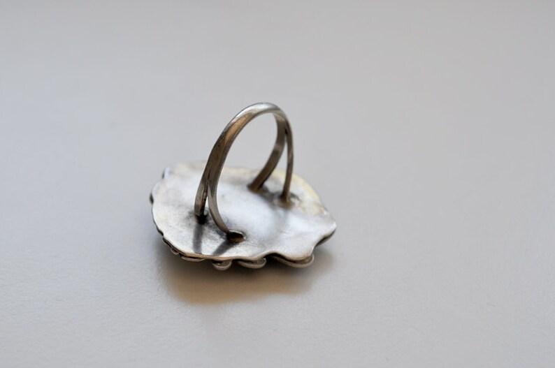 May include: Silver ring with a detailed design on the front. The back of the ring is plain and shows the band.