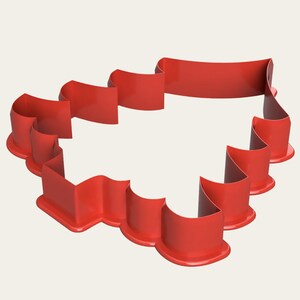 May include: A bright red cookie cutter in the shape of a banner. The cutter has a wavy design with a flat base and a curved top, perfect for creating decorative cookies or fondant shapes. The cutter is made of a shiny, smooth material.