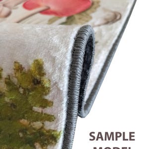 May include: A rolled-up rug with a botanical print featuring red mushrooms and green foliage. The rug has a white background and a gray border. The text "SAMPLE MODEL" is visible on the rug.