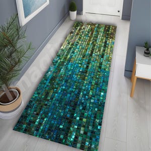 Op de afbeelding: Een rechthoekig gangtapijt met een mozaïektegelontwerp in tinten van teal, groen en goud. Het patroon van het tapijt loopt over van goud naar teal, waardoor een gradiënteffect ontstaat. Het tapijt ligt op een lichtgekleurde houten vloer.