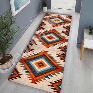 Pode incluir: Um tapete corredor retangular com um padrão geométrico em tons de laranja, verde-azulado, castanho e creme. O design apresenta formas de diamante e bordas em zigue-zague, adequado para um corredor ou entrada.