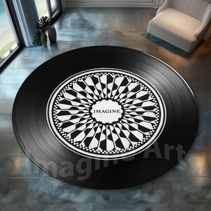 May include: A round black rug designed to resemble a vinyl record. The center features a white and black geometric pattern with the word "IMAGINE" in the center. The rug is on a tiled floor.