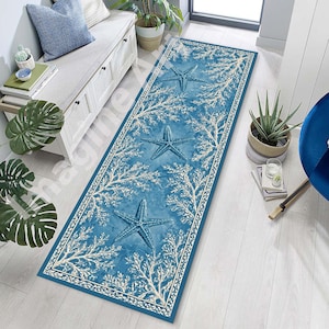 May include: A long, rectangular blue rug with a coastal theme. The rug features three raised blue starfish and white coral-like patterns against a textured blue background. The rug is bordered with a white and blue design.
