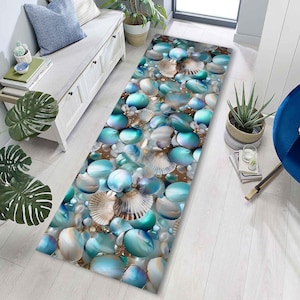 Può includere: Un tappeto rettangolare con un design a tema spiaggia. Il tappeto presenta un motivo di pietre blu e bianche, conchiglie e perle. La tavolozza dei colori include sfumature di blu, bianco e beige, creando un'estetica costiera.