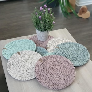Könnte beinhalten: Ein Set mit sechs gehäkelten Platzsets in verschiedenen Grüntönen und Rosa. Die Platzsets sind rund und haben ein strukturiertes, gewebtes Design.