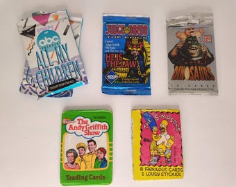 May include: A collection of vintage trading card packs featuring various television shows and characters. The packs include "All My Children," "Judge Dredd," "Dinosaurs," "The Andy Griffith Show," and "The Simpsons."