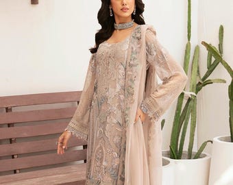 May include: A beige embroidered formal dress with matching pants and a sheer shawl. The dress features intricate floral patterns and is paired with gold-colored high-heeled sandals. The outfit is suitable for special occasions.