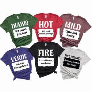 Könnte beinhalten: Eine Sammlung von sechs T-Shirts in verschiedenen Farben, jedes mit einem anderen Textdesign. Die Shirts sind grün, rot, kastanienbraun, blau, schwarz und grau. Der Text auf den Shirts lautet "DIABLO", "HOT", "MILD", "VERDE", "FIRE" und "FIRE ROASTED".