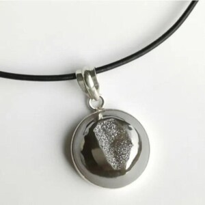 Peut inclure: Un collier pendentif argenté avec un cadre circulaire argenté poli. Le pendentif présente un centre argenté texturé et scintillant, suspendu à un cordon noir. Le collier est un bijou simple et élégant.