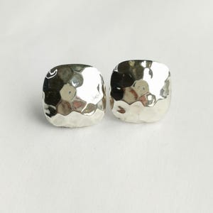 May include: A pair of square-shaped stud earrings with a polished silver-tone finish. Each earring features a distinct hammered texture across the front surface, creating multiple reflective facets that catch the light with a bright metallic sheen.
