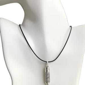May include: A silver-toned cylindrical pendant featuring a repeating spiral pattern, suspended from a simple black cord. The pendant has a metallic finish with vertical textured detailing along the sides and a small loop at the top for attachment.