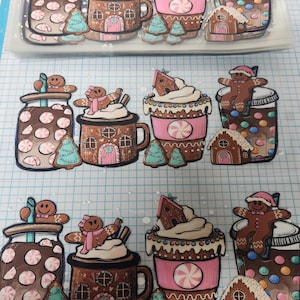 May include: A collection of die-cut stickers featuring festive holiday designs. The stickers include gingerbread men, gingerbread houses, mugs of hot chocolate, and jars filled with candies. The color palette includes brown, pink, white, and teal.