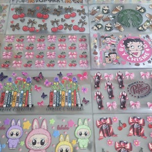 May include: A collection of clear sticker sheets featuring various designs. These include cherries, bows, butterflies, cartoon characters, and text such as "CHAPTER" and "labubu". Some stickers have a floral theme, and others feature Dr. Pepper cans.